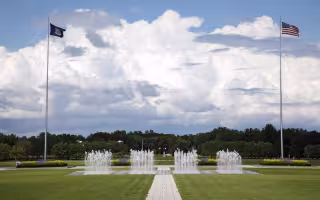 Flags wave in the wind and fountains spray water in the UAlbany entry plaza.