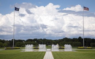 Flags wave in the wind and fountains spray water in the UAlbany entry plaza.