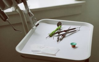 White plastic tray of dental implements including white gauze pads, various metal picks, and a small container of fluoride with a green metallic cap