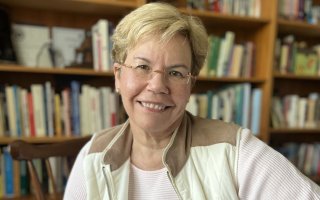 A smiling woman in glasses in front of a bookcase.