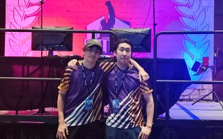 Josh Pressano and Kenta Lange stand in front of the game stage in their UAlbany Esports jerseys at the Collegiate Esports Commissioner’s Cup. 