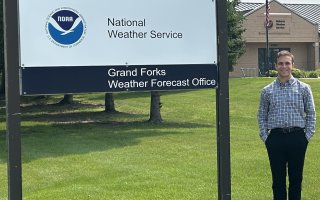 Daniel Harkin stands next to a Grand Forks Weather Forecast Office sign.