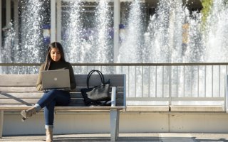 Student on laptop sitting on a bench in front of fountain