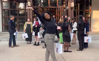 Alissa Banfield poses with a bag in one hand and an arm in the air outside of a building where a crowd has gathered.