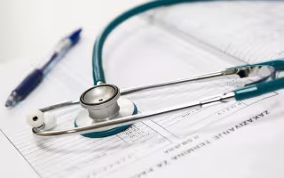 A blue stethoscope and a blue pen are laid on top of a medical spreadsheet