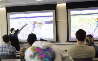 A UAlbany atmospheric science student points to a weather map of the United States.