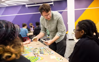 Jason Corace holds playing cards while interacting with students in his Game 100 course.