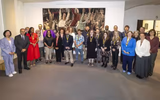 More than 2 dozen smiling people, many wearing medalions, stand in a semicircle in front of a large painting