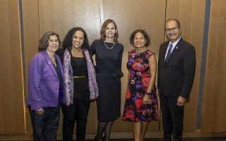 Four people dressed in business attire pose together for a group portrait in front of a wood-paneled wall.