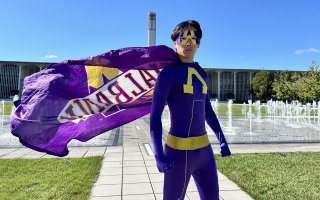UAlbany Man stands in his purple and gold uniform at the University Entry Plaza.