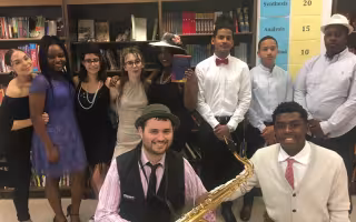 A group of people in 1920s attire pose for a photo. One is holding a saxophone and another is holding The Great Gatsby book.