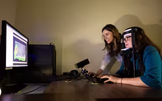 A woman in an apparatus looks at a monitor measuring where her line of sight goes as anothe woman looks on.