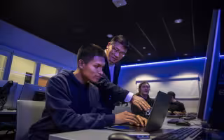 Alan Wang works with a student on his class project from the Cyber Range lab.