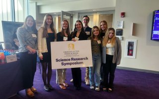 Students from Saratoga Springs High School hold up a Science Research Symposium sign inside UAlbany's Campus Center.