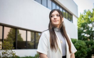 Student Cassie Kane stands in front of the School of Public Health, looking to the side.