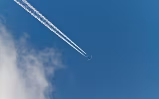 Thin white clouds form behind a jet across the sky.