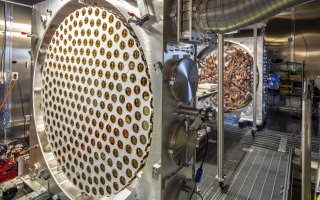 A large circular, sophisticated device is surrounded by aluminum with tiny brass coils and wiring.