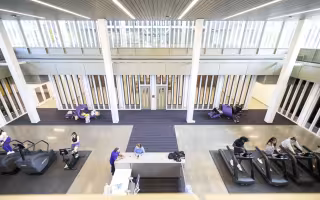 A large, light-filled room with vertical windows, a large check-in desk and a variety of exercise machines.