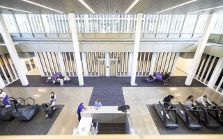 A large, light-filled room with vertical windows, a large check-in desk and a variety of exercise machines.