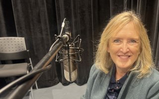 A smiling woman in a gray jacket sits next to a microphone