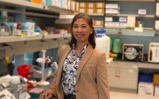 A woman in a beige blazer and floral blouse smiles, posing for a portrait, in a biology lab. 