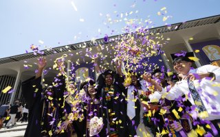 Students in caps and gowns celebrate as purple and gold confetti rain down on them at UAlbany's commencement ceremony.