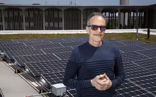 Richard Perez stands with sun glasses on in front of solar panels on top of UAlbany's Campus Center.