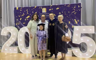 A family from Mongolia surrounds a man dressed in doctoral robes in front of a 2025 sign and a purple backdrop of the University at Albany.