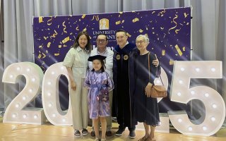 A family from Mongolia surrounds a man dressed in doctoral robes in front of a 2025 sign and a purple backdrop of the University at Albany.