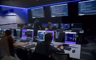 Students review code on a row of computers inside a dark lit room at ETEC.