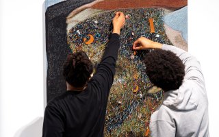 Two young African American students work with a fabric art piece in the University Art Museum by artist Noel W Anderson.