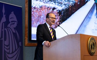 A man in a stiped tie speaks at a lecturn