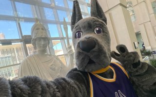 UAlbany'e mascot Damien the Great Dane takes a selfie with the statue of Minerva, framed in windows.