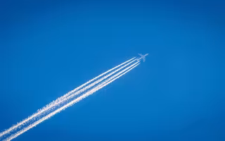 White smoke trails behind an aircraft in the blue sky.
