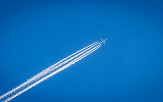 White smoke trails behind an aircraft in the blue sky.