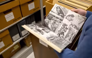 Photo of person holding yearbook opened to a page of photos in the stacks