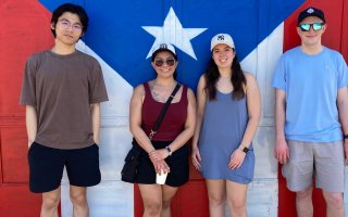 UAlbany students stand for a photo in front of a painting of the Puerto Rican flag.