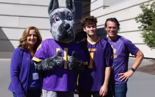 A mom, a Great Dane mascot, a college-aged son and a dad stand in a row in front of a building