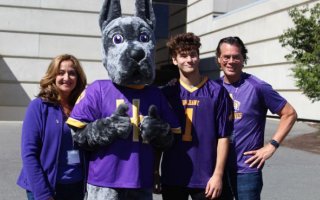 A mom, a Great Dane mascot, a college-aged son and a dad stand in a row in front of a building