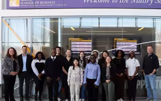 A group of people stand inside the Massry School of Business at the Unviersity at Albany posed for a group shot.