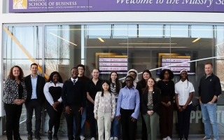 A group of people stand inside the Massry School of Business at the Unviersity at Albany posed for a group shot.