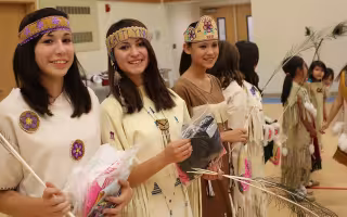 A group of Alaska Native young women and girls perform a traditional cultural dance in a gym wearing traditional attire.