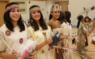 A group of Alaska Native young women and girls perform a traditional cultural dance in a gym wearing traditional attire.