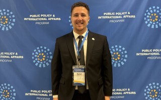 Dylan Repertorio stands in a suit wearing a Public Policy and International Affairs Junior Summer Institute credential.