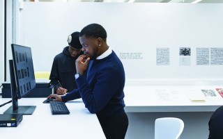 Two students view an archive of materials in a white study space with a sign that reads Romare Bearden & Ralph Ellison: From the Archive on the wall behind them.