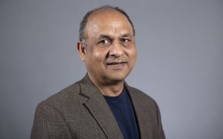 A portrait of UAlbany physicist Vivek Jain wearing a brown jacket and blue shirt.