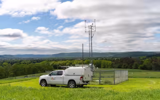A NYS Mesonet truck sits in front of a site in the Adirondacks.