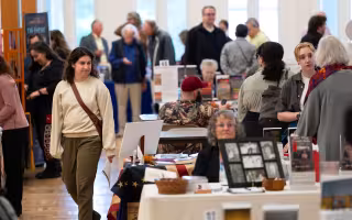 People seated at tables show off their books as others move among the tables at a book festival at UAlbany