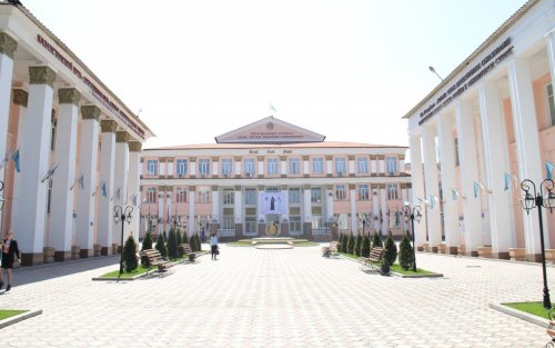 The Kazakh National Medical University building is white with large white columns and pale salmon-colored accent walls. In front of the building is a white-brick courtyard.