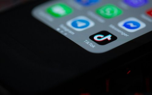 Image is mainly black, showing a corner of a glowing smartphone with several icons for apps including TikTok.